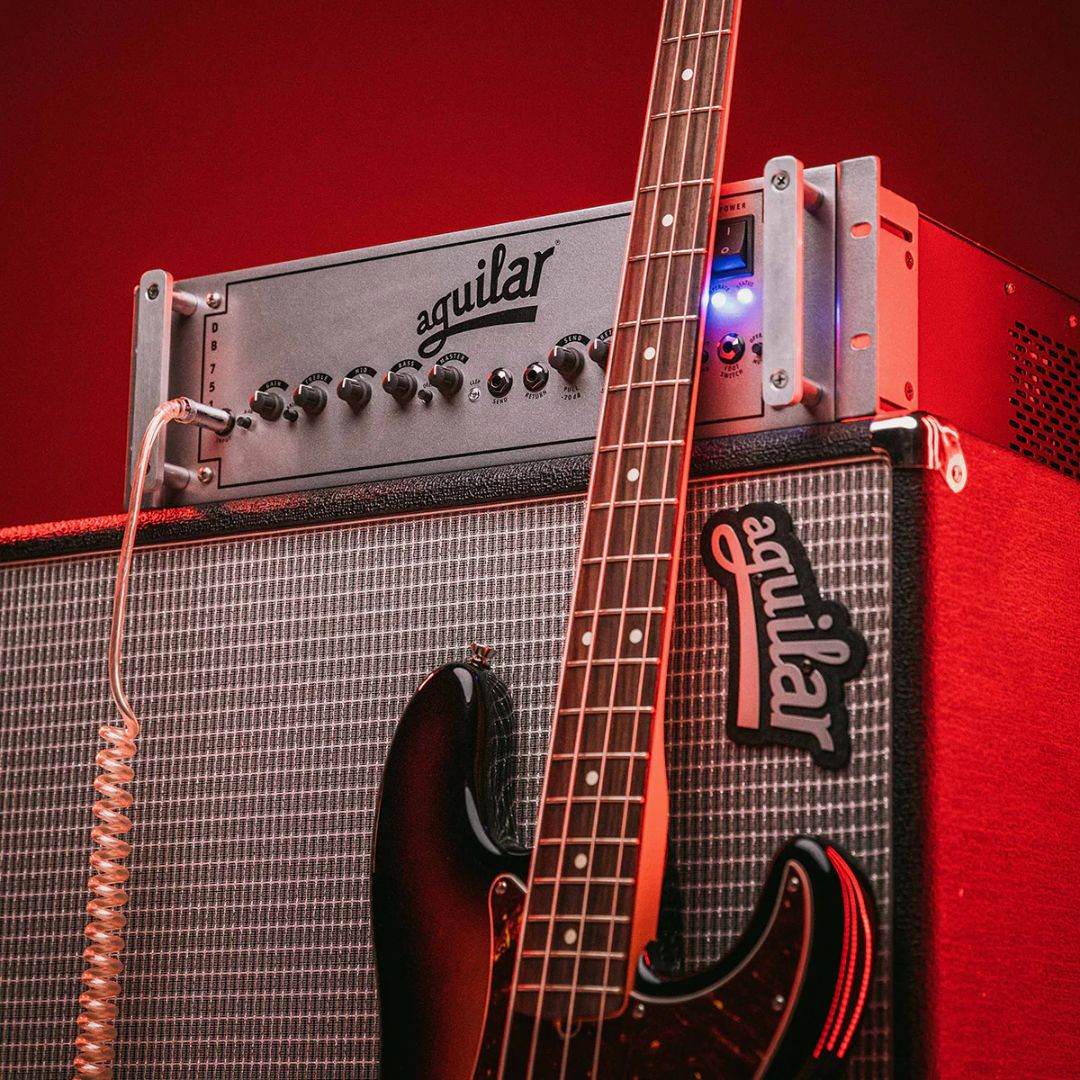 Angled front view of Aguilar DB 751 Bass Amp Head on top of speaker cab with bass leaning on it in red-lit studio