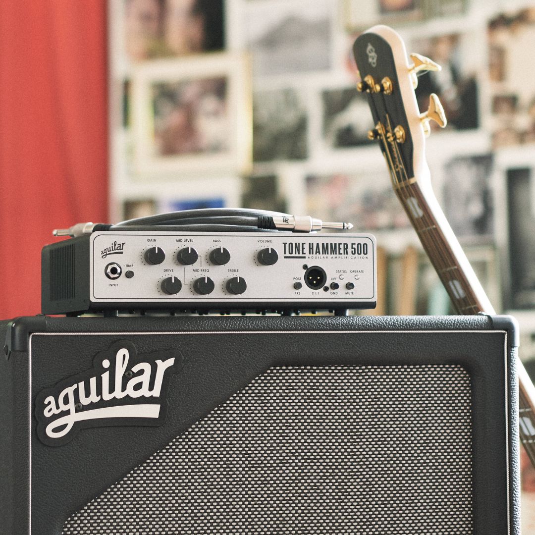 Angled front view of Aguilar Tone Hammer 500 Bass Amp Head on top of speaker cab with bass leaning on it in studio
