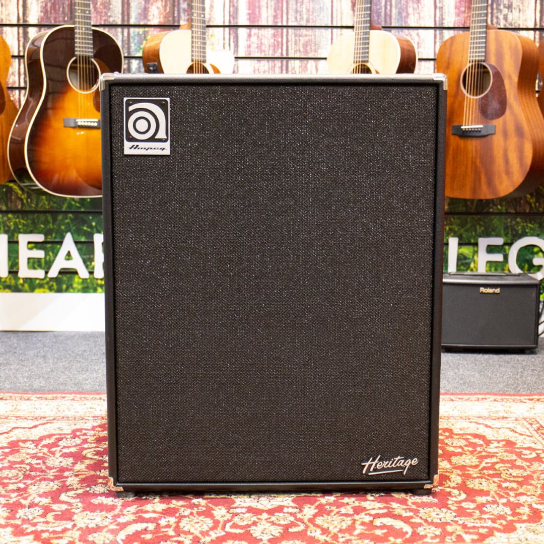 Front view of Ampeg HSVT-410HLF Heritage 4x10" 500W Bass Cabinet on red carpet with guitars hanging in the background