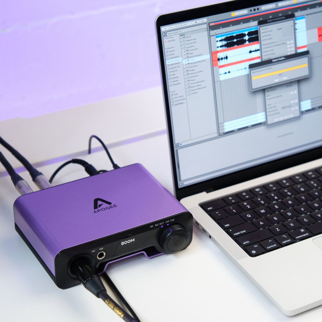 Purple audio interface device connected to a laptop with music software open on a white surface.