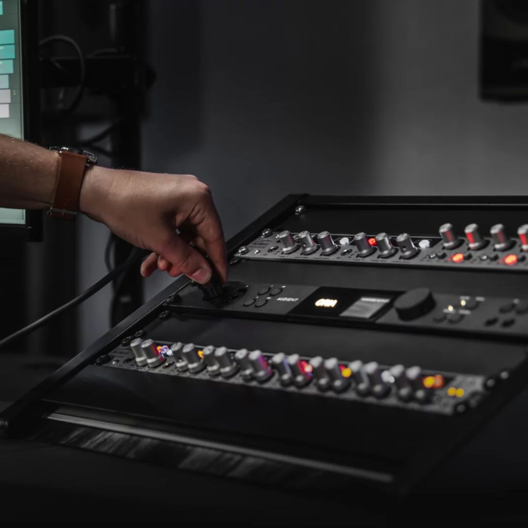 Angled side view of Audient ORIA in an equipment rack with a hand plugging a cable into its input with other rackmount effects in view inside a studio