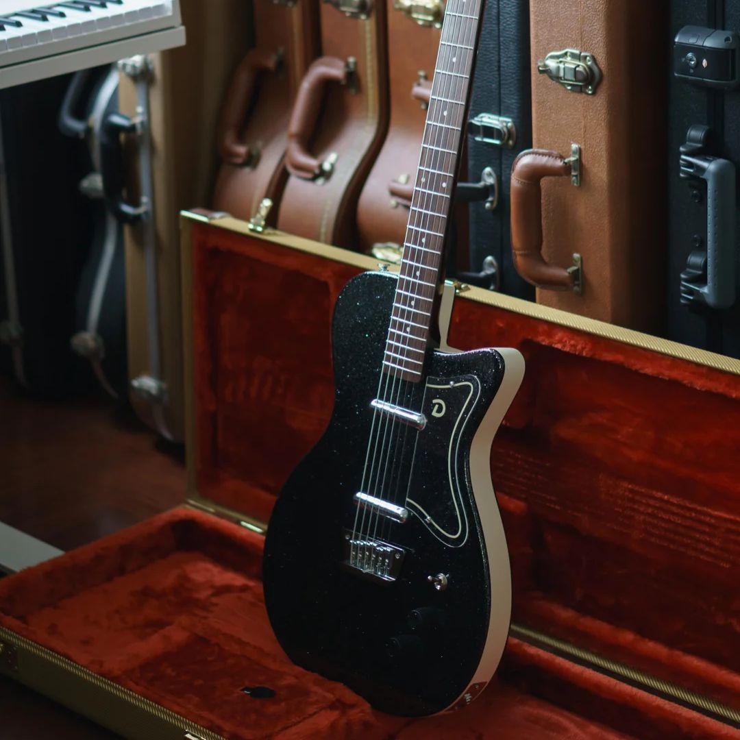 Close up angled view of Danelectro 56 Baritone Electric Guitar Black Metal Flake on hardcase with hardcases in the background