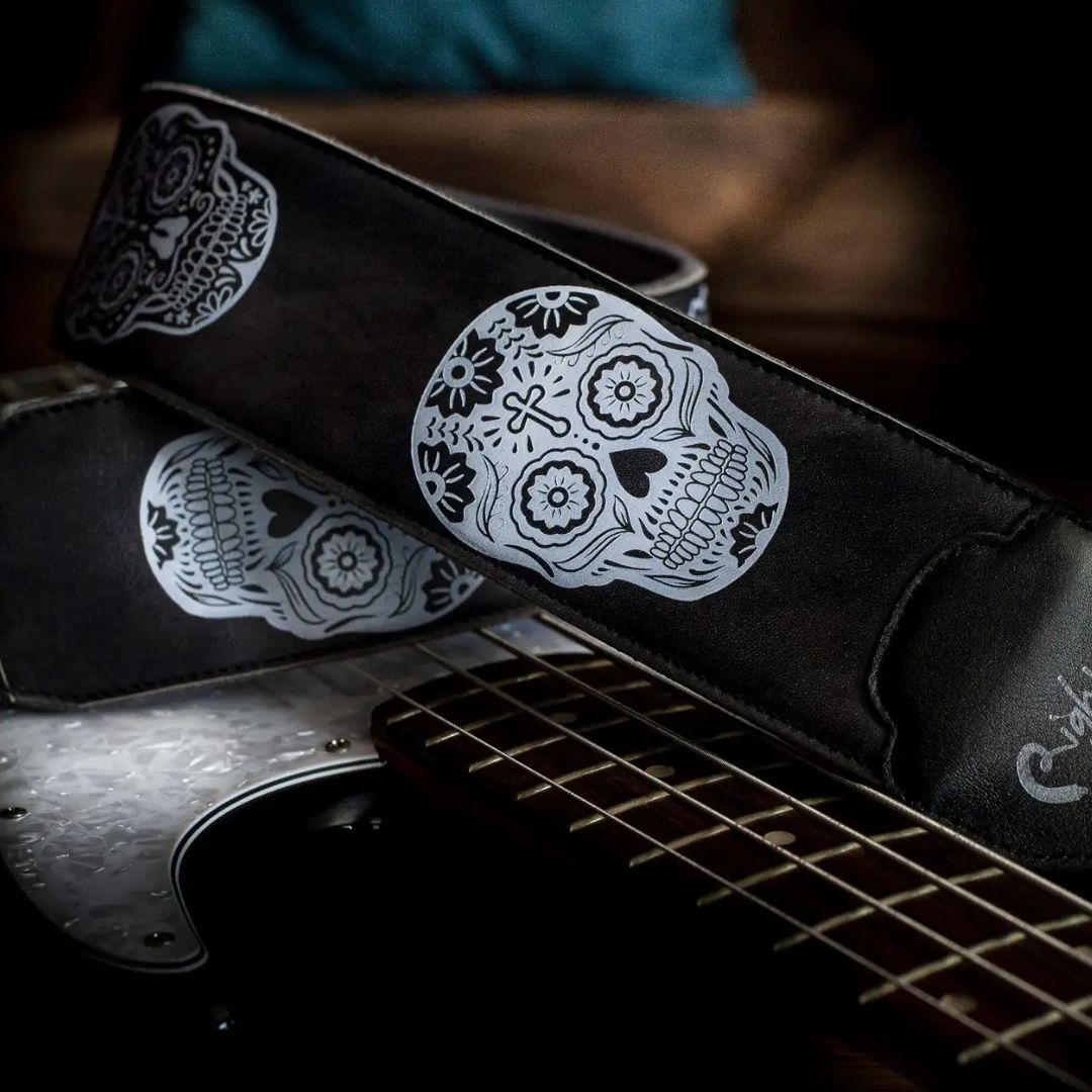 Curled view of RightOn Sugar Skulls Guitar Strap Black on top of guitar with brown couch background
