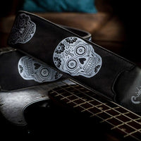 Curled view of RightOn Sugar Skulls Guitar Strap Black on top of guitar with brown couch background