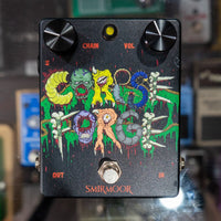 Front view of Smirmoor Corpse Forge Pedal on glass cabinet with various guitar pedals in the background