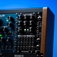 Front view of Strymon SuperKar+ 32 Voice String Synthesis Eurorack Module on synth rack with other modules beside it with blue background