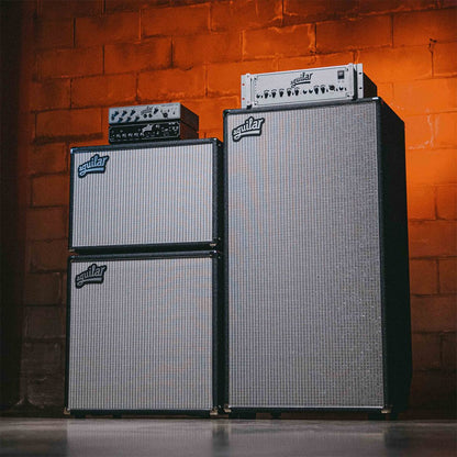 Angled view of Aguilar DB 810 Bass Cabinet on the right with various Aguilar speaker cabs and amp heads on the left with brick wall background