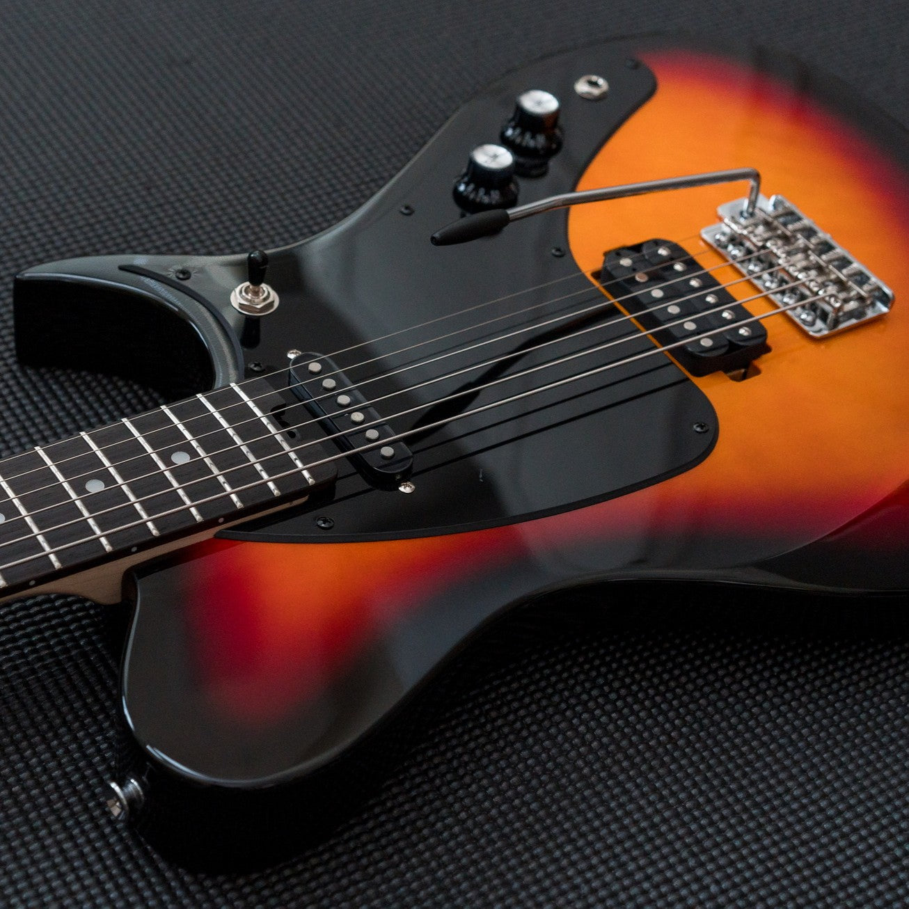 Angled close up view of Aria Pro II J-B’tone Electric Baritone Guitar 3-Tone Sunburst on black surface