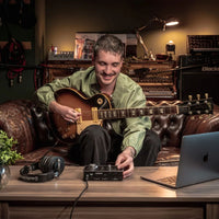 Guitarist on couch in studio with laptop, Audient iD14 MKII, and headphones on a table