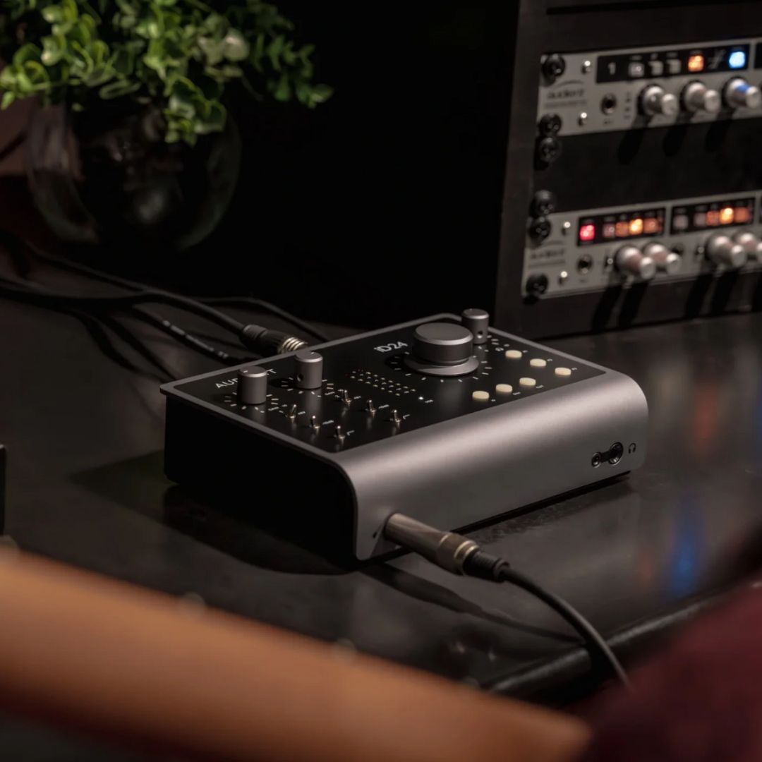 Angled front view of Audient iD24 on studio desk with cables attached and a guitarist in the foreground