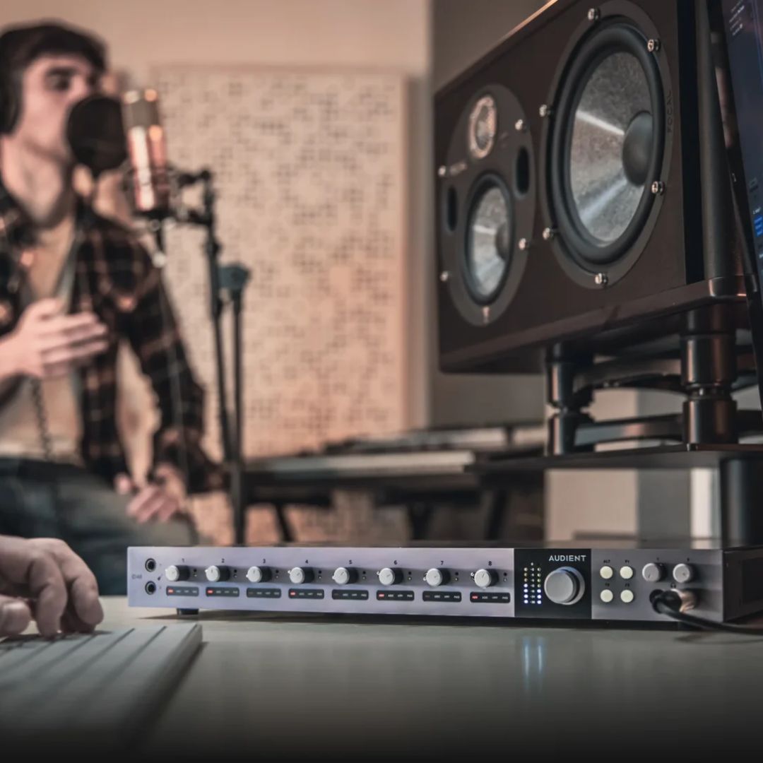Angled front view of Audient iD48 on studio desk while recording vocalist in the background