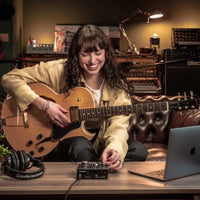 Guitarist on couch recording guitar on Audient iD4 MKII with laptop and headphones on desk in studio