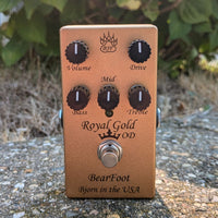 Front view of BearFoot FX Royal Gold OD pedal on roadside with leaves in the background