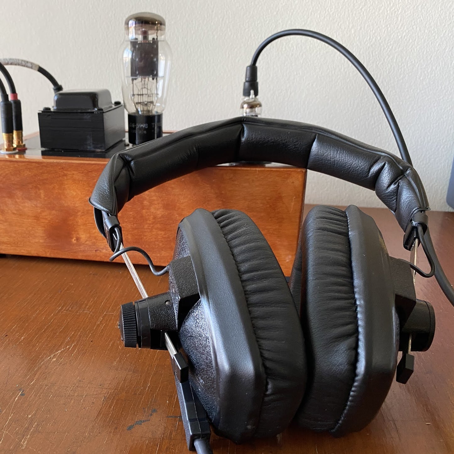 Angled bottom view of Beyerdynamic DT 100 Closed-Back Headphones (400 Ohms) on wooden surface with DI box in the background