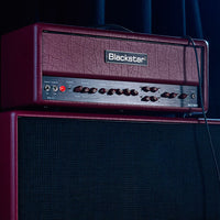 Angled front view of Blackstar DA100 Doug Aldrich Ruby 100W Guitar Amp Head on top of speaker cabinet in dim-lit venue