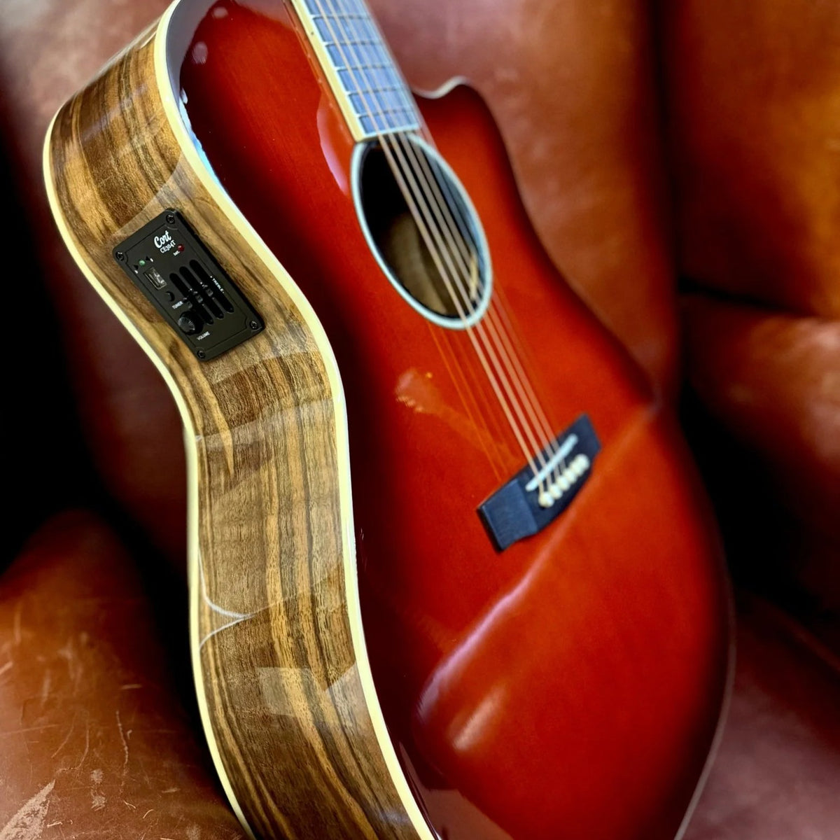 Close up angled view of Cort Exotic-GA Walnut Acoustic Electric Guitar on brown couch