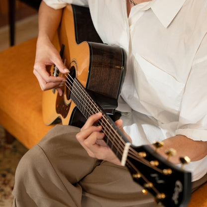 Guitarist playing the Cort Gold-MC6 Ovangkol Acoustic Electric Guitar (Natural Gloss) while on orange couch in room