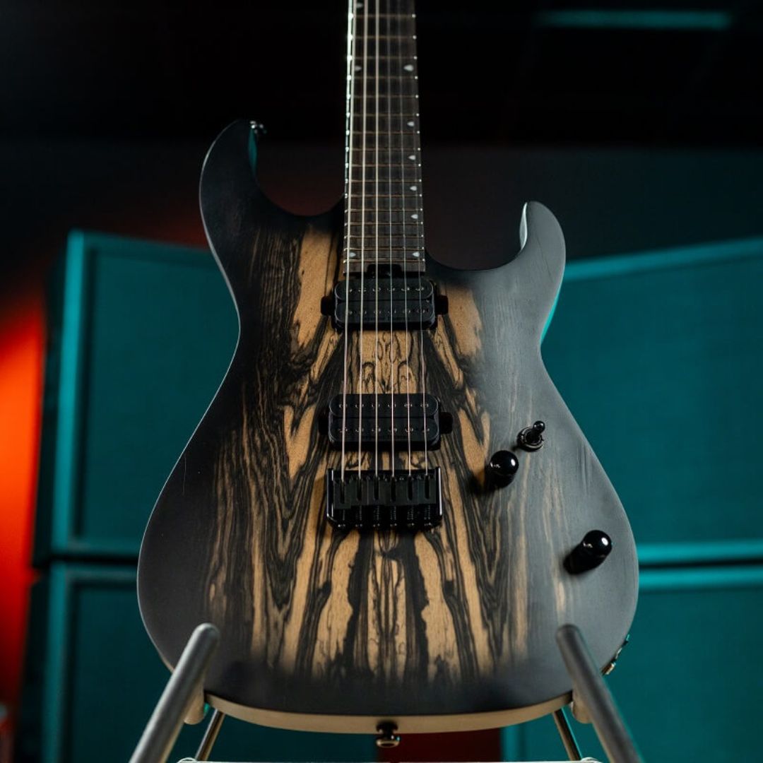 Close up front view of Cort KX500 Pale Moon Electric Guitar on stand with amplifiers in the background in studio