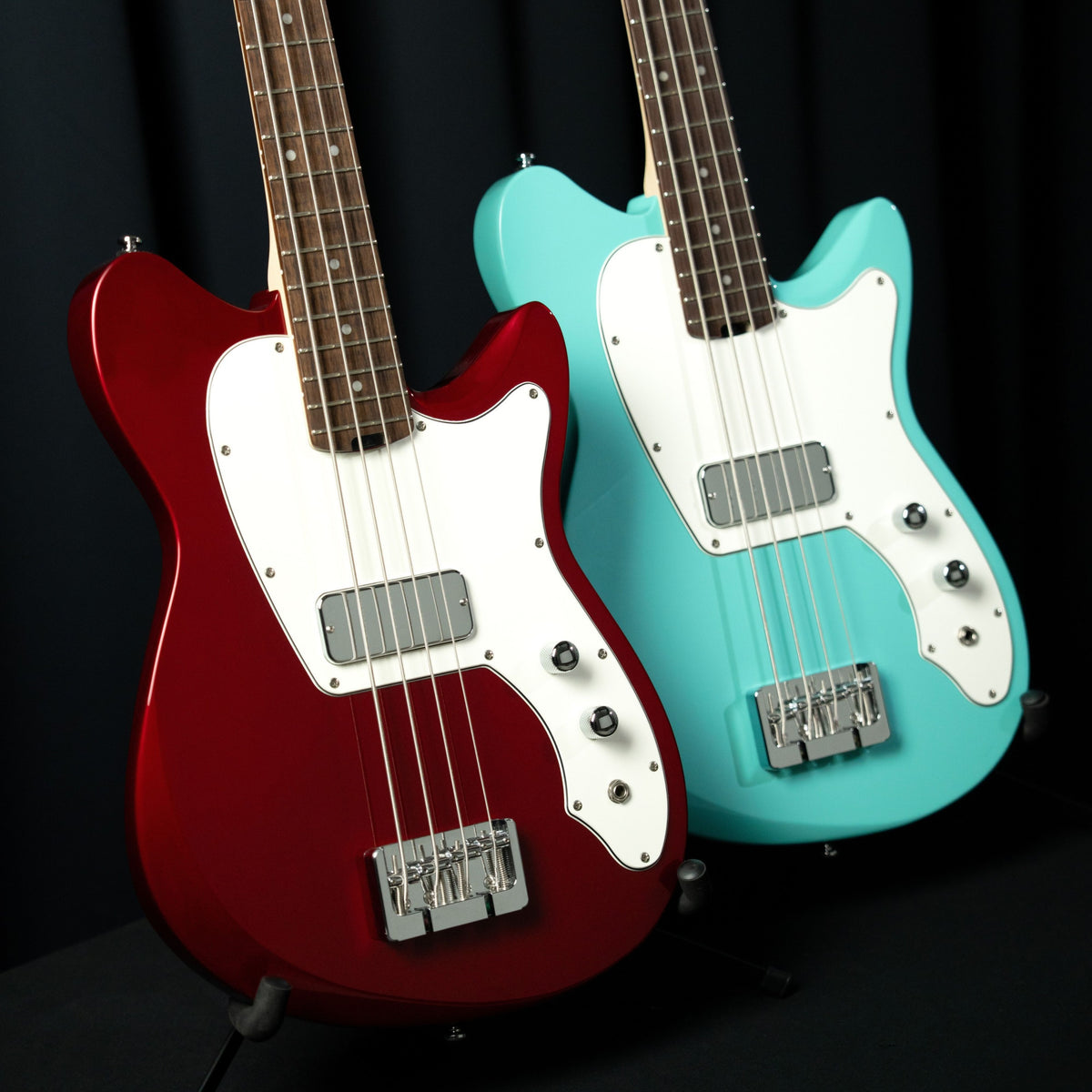 Close up view of Cort Retro 304 Short Scale Electric Bass Guitar Candy Apple Red and Seafoam Green side by side in studio