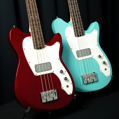 Close up view of Cort Retro 304 Short Scale Electric Bass Guitar Candy Apple Red and Seafoam Green side by side in studio