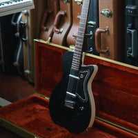 Close up angled view of Danelectro 56 Baritone Electric Guitar Black Metal Flake on hardcase with hardcases in the background