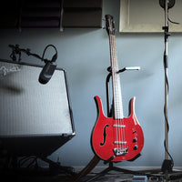 Danelectro 58 Longhorn Bass Guitar Red on stand with amplifier on the side in studio