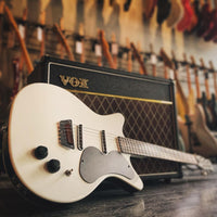 Angled close up view of Danelectro PB Special Semi Hollow Electric Guitar White leaning on amplifier with guitars in the background
