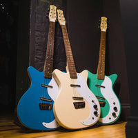 Angled view of Danelectro Stock 59 Electric Guitar Vintage Cream, Aquamarine, and Vintage Aqua leaning on black wall with wooden flooring
