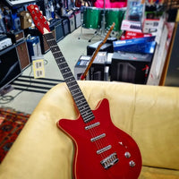 Danelectro Triple Divine Electric Guitar Red on beige couch inside music store