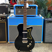 Front view of Danelectro '56 U2 Electric Guitar (Black) with guitar amplifiers in the background