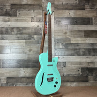Angled front view of Danelectro '56 Vintage Baritone Electric Guitar Aqua with wooden wall background