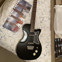 Close up view of Danelectro '57 Electric Guitar Limo Black on bed with box and Danelectro flyer beside it