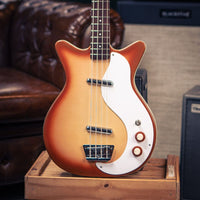 Close up front view of Danelectro '59DC Long-Scale Bass Guitar Copper Burst on wooden crate with amplifier and couch in the background