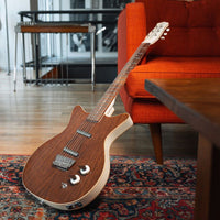 Angled view of Danelectro '59 Divine Electric Guitar Dark Walnut leaning on red couch in living room