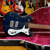 Close up view of Danelectro '66BT Baritone Electric Guitar Transparent Blue leaning on guitar hardcase with other guitars in the background