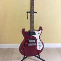 Close up front view of Danelectro '66 Electric Guitar Transparent Red on guitar stand with yellow background