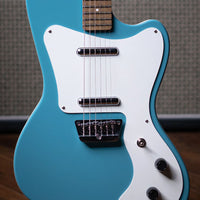 Close up front view of Danelectro '67 Electric Guitar Aqua with amplifier in the background on wooden floor