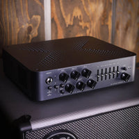 Angled front view of Darkglass Microtubes X 900 Bass Amplifier Head on top of speaker cab with wooden background