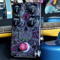 Angled top view of Flattley DG Fuzz Pedal on black surface with guitars in the background