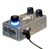 Angled side view of Flattley The Ace Tone Boost Pedal with power cable attached on white background