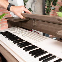Close-up of a person opening a wooden piano lid with a keyboard visible.