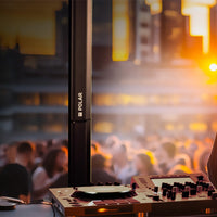 Rear view of Polar MKII speaker with DJ controller in foreground and partying crowd and buildings in the background