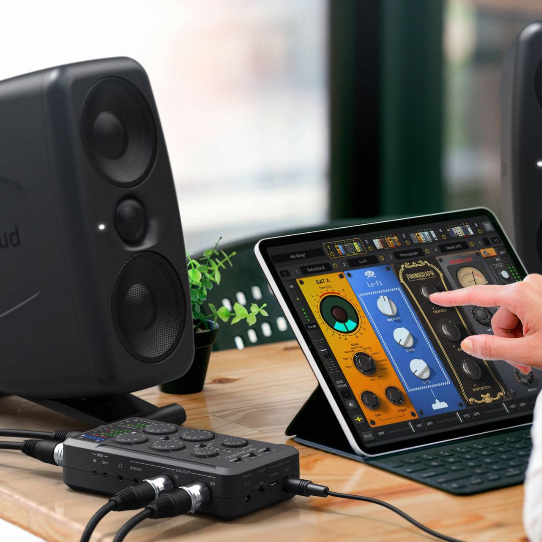 Person using a tablet with music software on a desk with speakers and audio equipment.