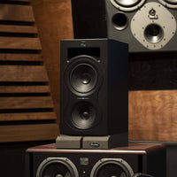 Pair of speakers on a wooden stand with a wooden wall background