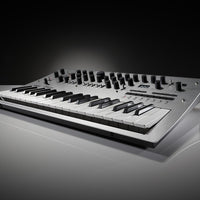 Angled front view of Korg minilogue Polyphonic Analogue Synthesizer on white surface with dark background