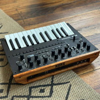 Angled rear view of Korg monologue Monophonic Analogue Synthesizer Black on beige carpet on wooden floor