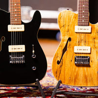 Two electric guitars, one black and one with a wood finish, on stands against a blurred background.