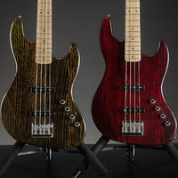 Two electric bass guitars, one with a black and gold finish and the other with a red finish, on stands against a dark background.