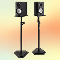 Front view of On-Stage Hex-Base Monitor Stands (Pair) with speakers mounted on yellow and orange background