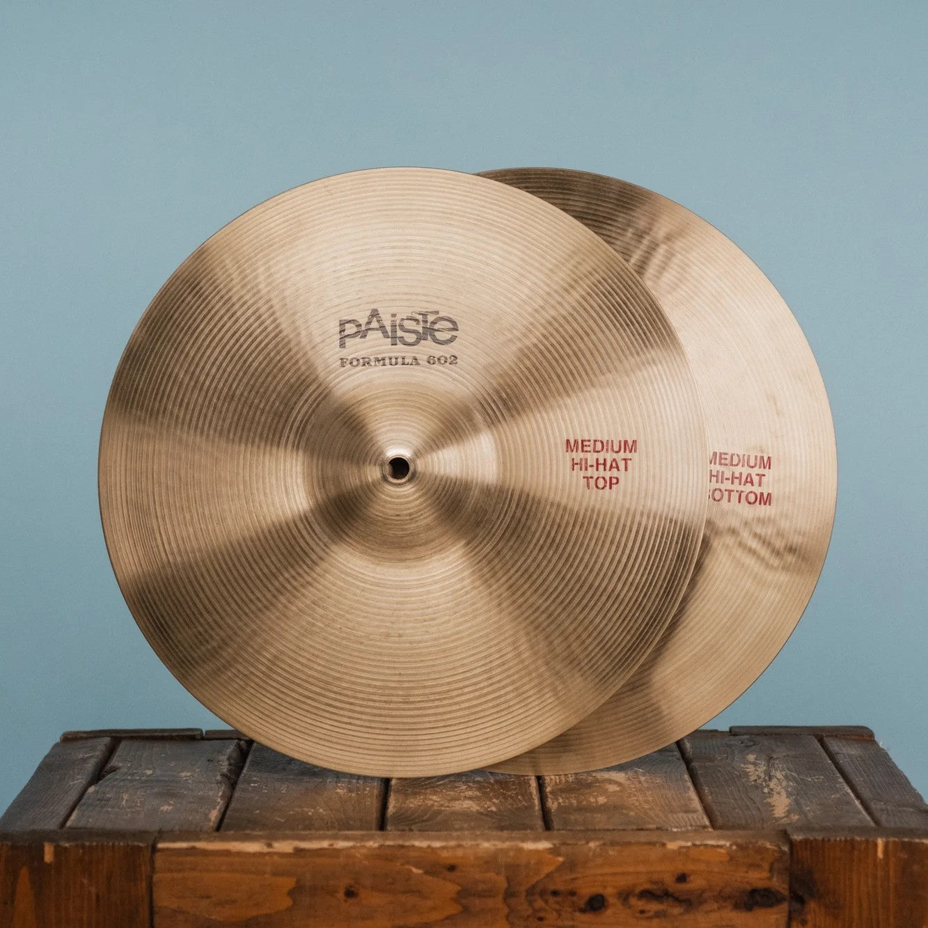 Front view of Paiste 14" Formula 602 Classic Medium Hi-Hats on wooden crate with blue background